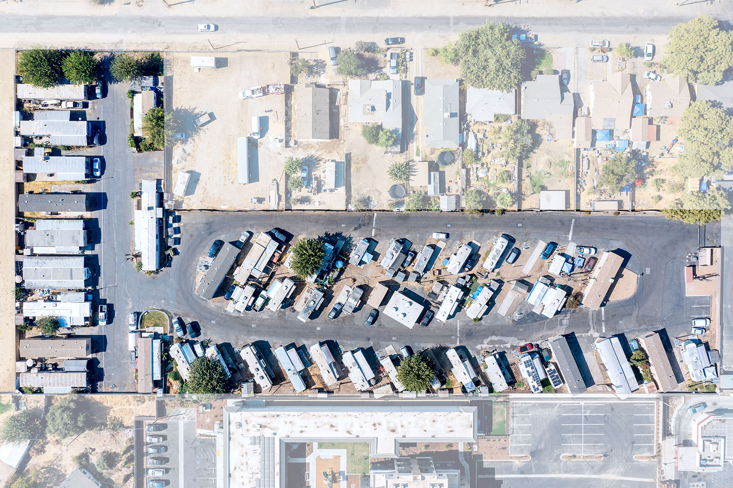 Aerial view of Park View Mobile Home & RV Park in Fresno, CA, showing rows of mobile homes and RVs parked on paved lots, surrounded by trees, vehicles, and nearby residential buildings.