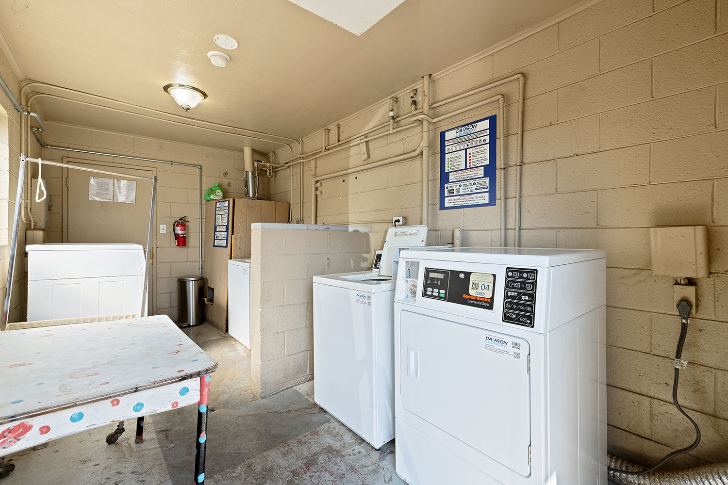 Laundry room at Park View Mobile Home & RV Park in Fresno, CA, featuring coin-operated washers and dryers, a folding table, and instructional signs on the wall.